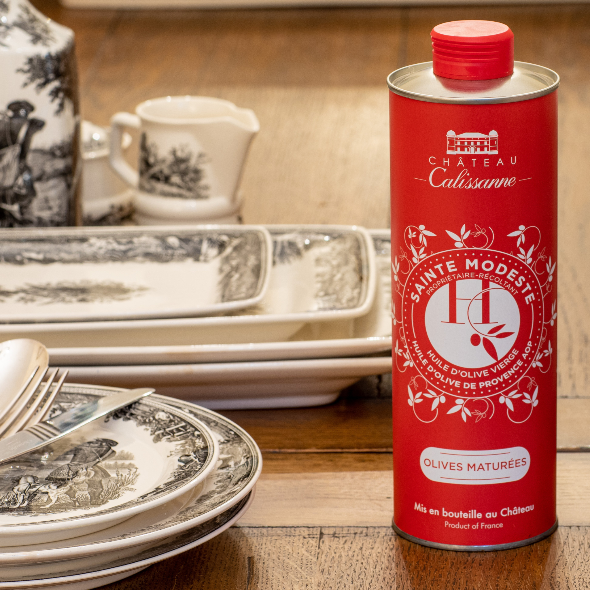 Kanister Olivenoel Sainte Modeste auf einem Holztisch neben antikem Geschirr
