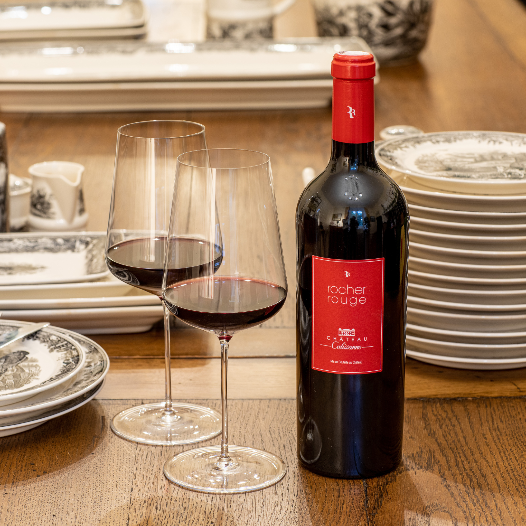 Eine Flasche Rocher Rouge Rotwein auf einem Holztisch mit Gläsern und Geschirr