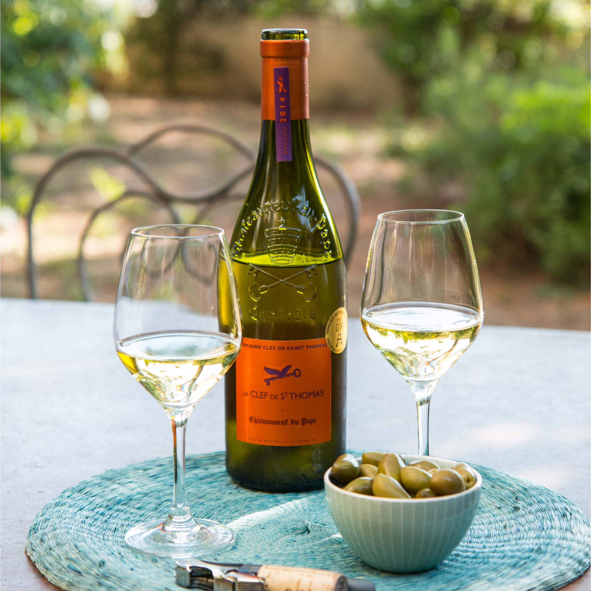 ine Flasche Weißwein Clef-Saint-Thomas-Chateauneuf-du-pape auf einem Tisch mit zwei Gläsern und Oliven. 
